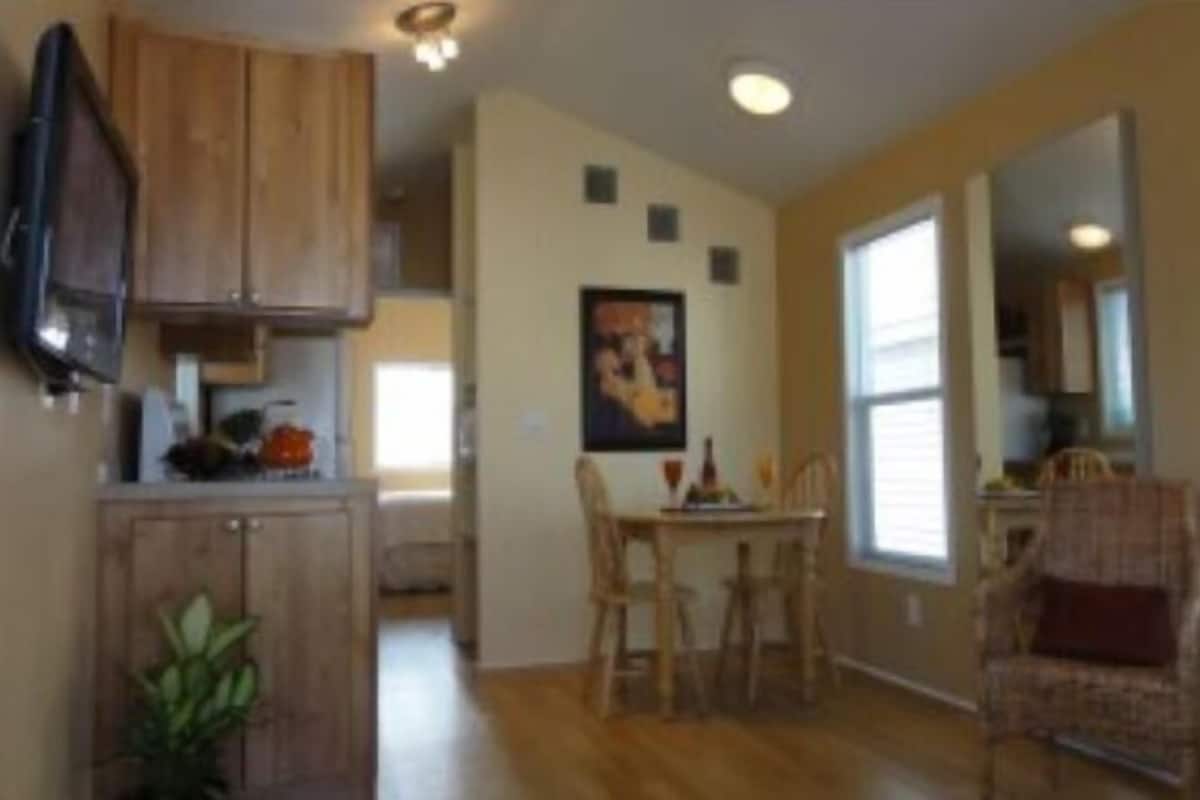 A dining area with wooden chairs and a table, a kitchen with wooden cabinets, and a painting on the wall.