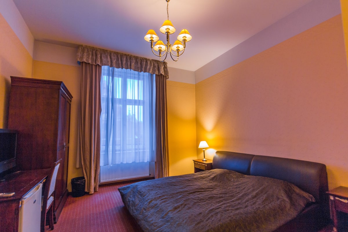 Ein Hotelzimmer mit einem Bett, einem Schreibtisch mit Computer, einem Fernseher, einer Lampe und einem Fenster mit Vorhängen.