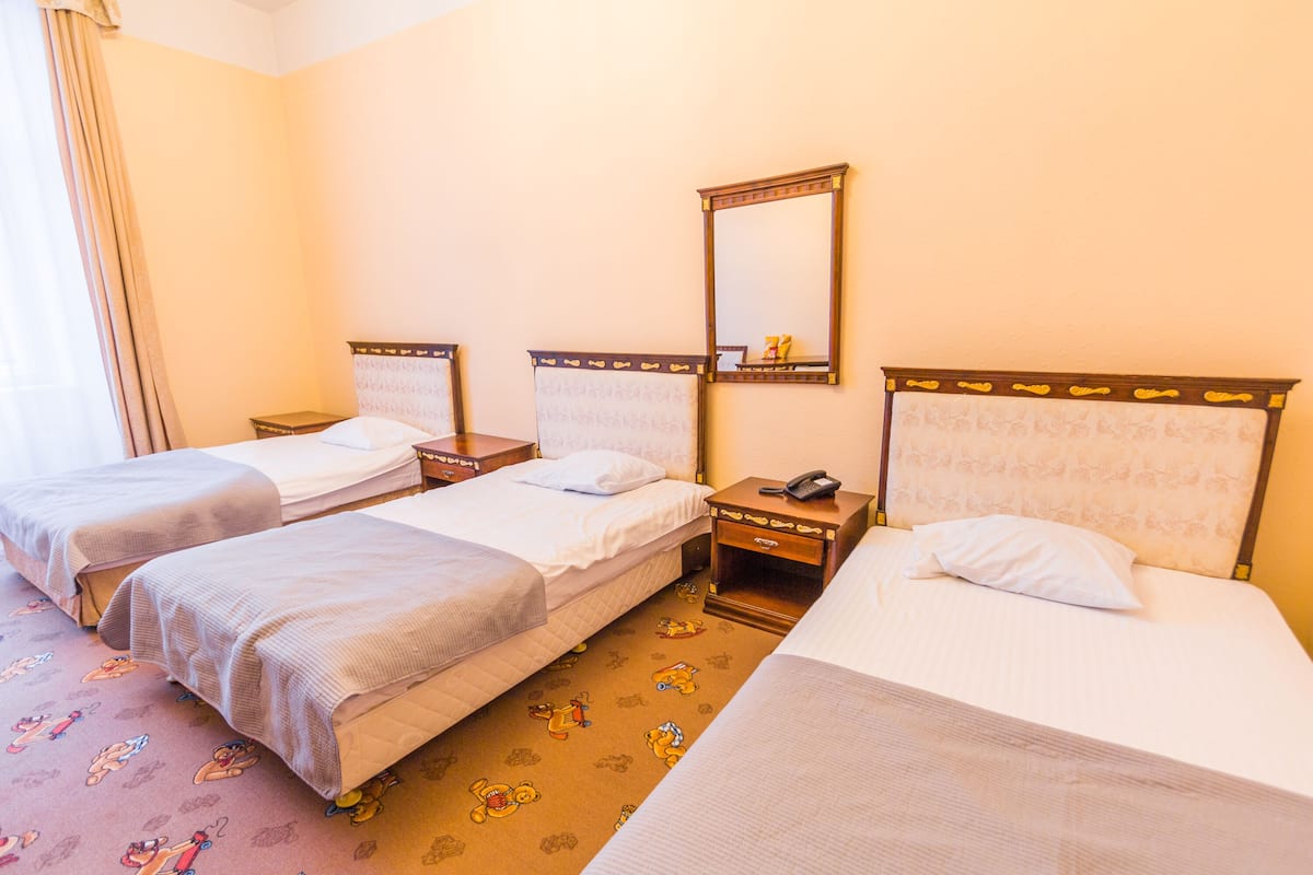 Ein Hotelzimmer mit drei Einzelbetten, einem Nachttisch mit Telefon und einem Spiegel an der Wand.