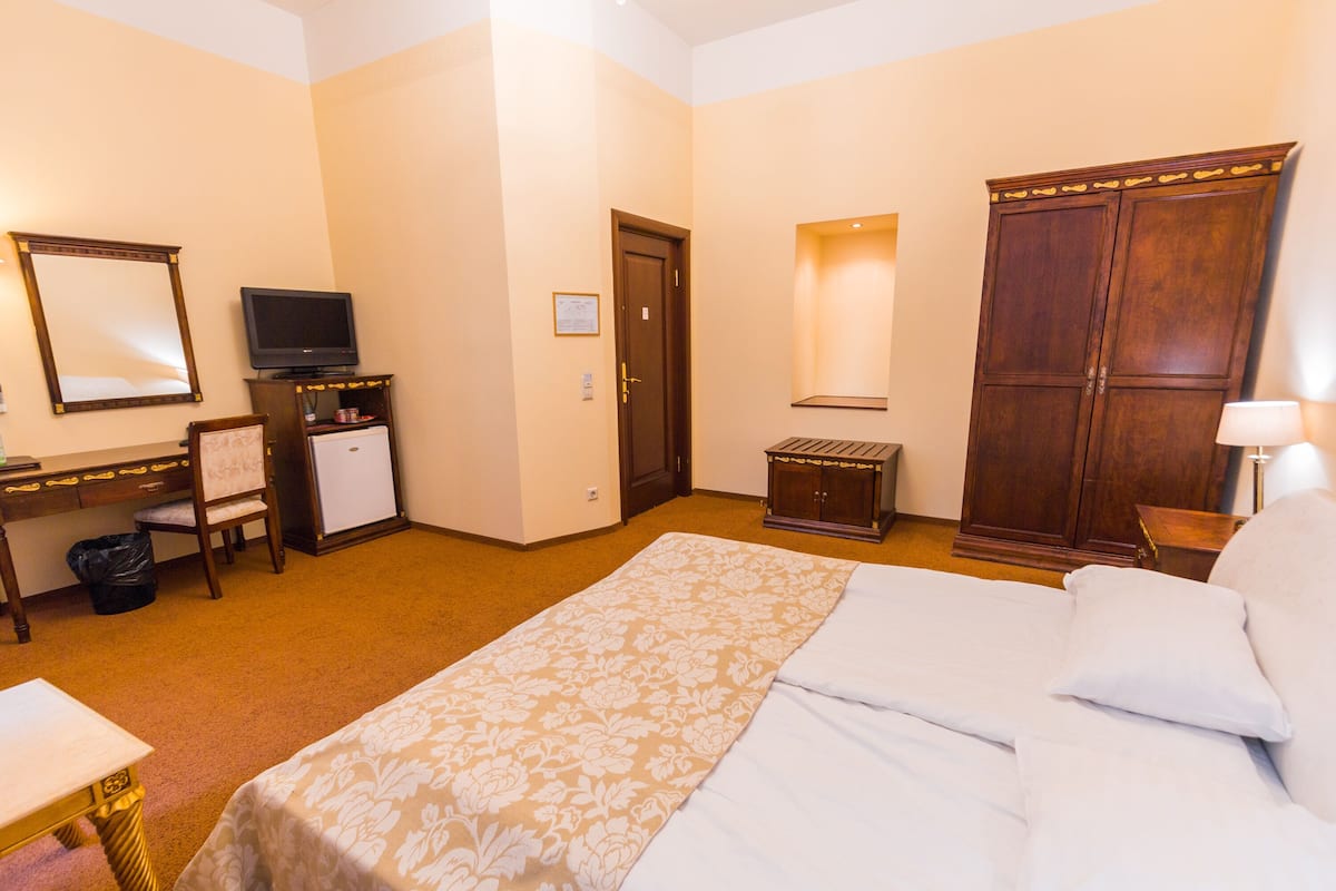 Ein Hotelzimmer mit einem Bett, einem Schreibtisch mit Computer, einem Fernseher und einem Kleiderschrank.
