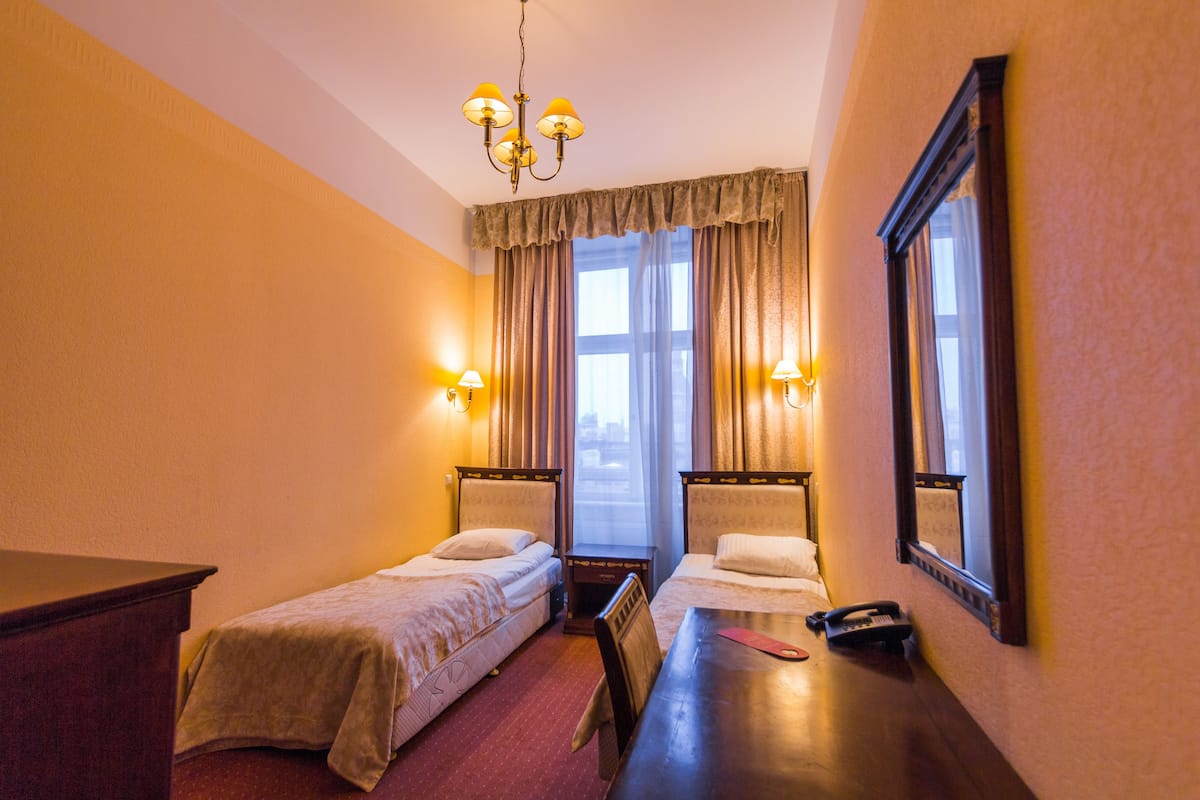 Ein Hotelzimmer mit zwei Einzelbetten, einem Holztisch, einem Telefon und einem Spiegel an der Wand.