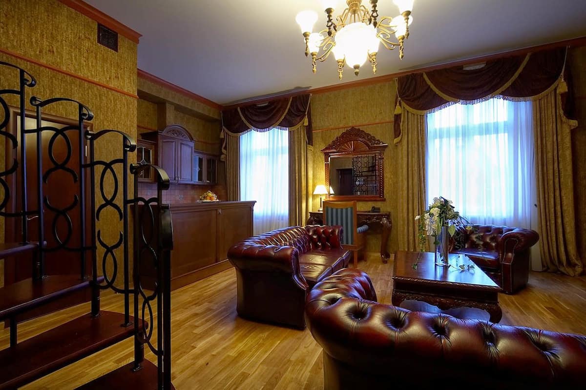 Ein traditionell eingerichtetes Hotelzimmer mit Holzboden, Ledersofas, einem Essbereich mit einer Chandelüster und einer Küche im Hintergrund.