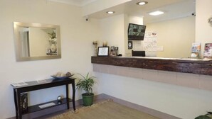 A reception area with a wooden counter, a mirror, a television mounted on the wall, and a small table with a plant. - Lotus of Lompoc - A Great Hospitality Inn (Lompoc)