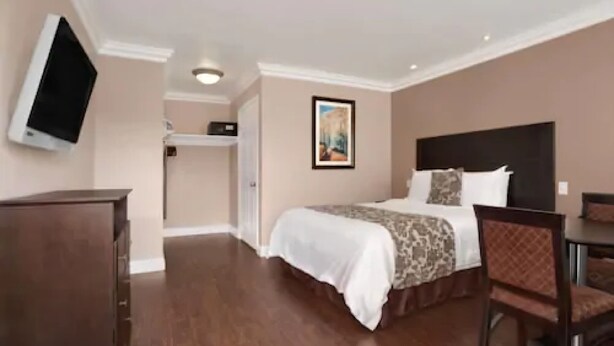 A hotel room with a bed, a desk, a chair, a television, and a painting on the wall. - Lotus of Lompoc - A Great Hospitality Inn (Lompoc)