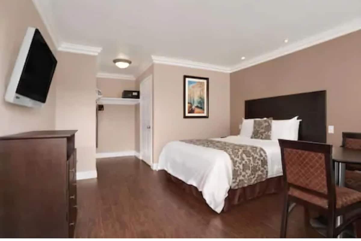 A hotel room with a bed, a desk, a chair, a television, and a painting on the wall.