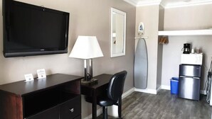 A hotel room with a TV, desk, chair, lamp, ironing board, and kitchenette. - Lotus of Lompoc - A Great Hospitality Inn (Lompoc)