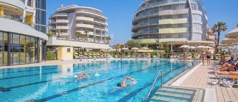 A swimming pool with multiple lanes, surrounded by modern buildings with balconies and outdoor seating.