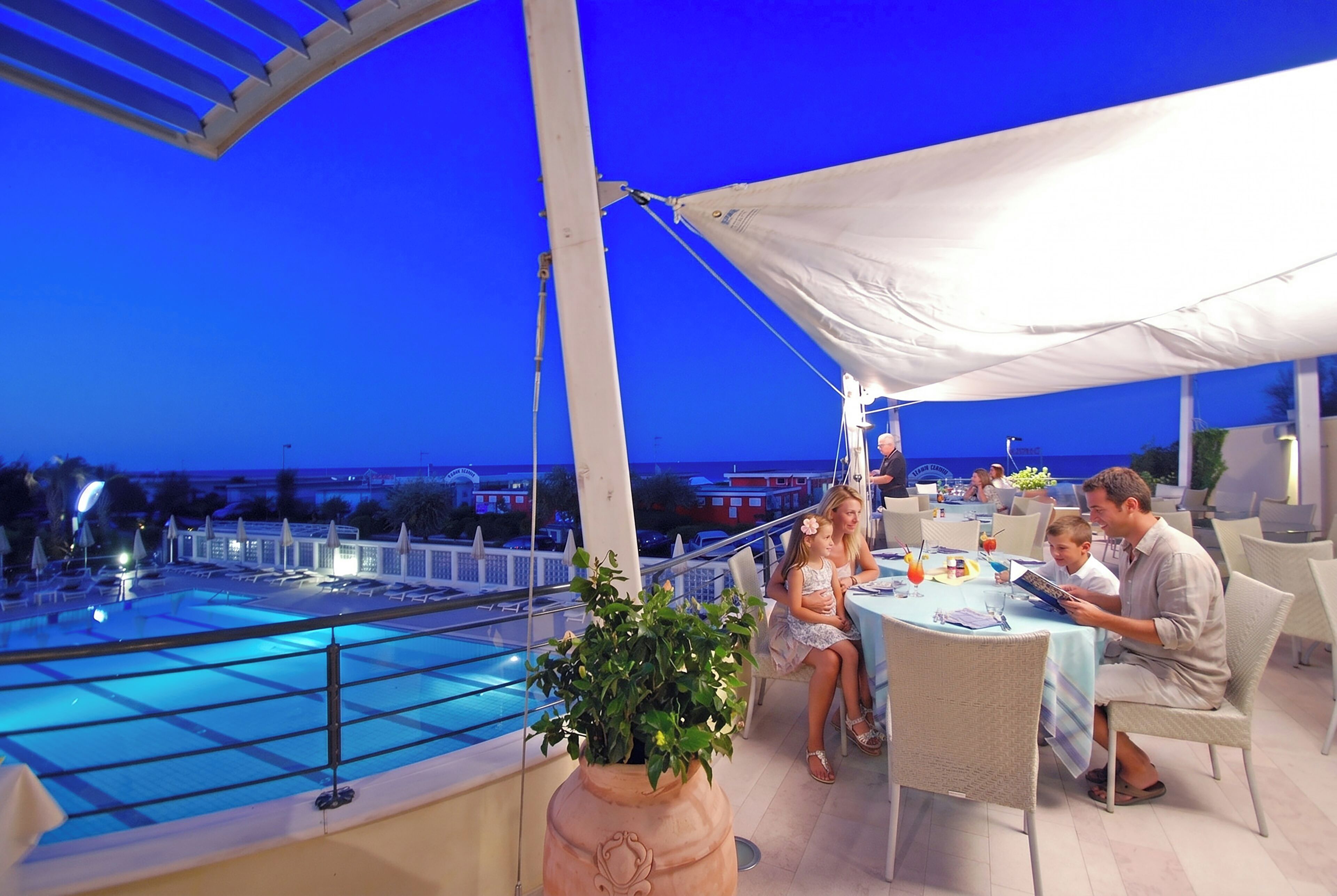 Zona junto a la piscina con mesa y sillas, una sombrilla grande y vista al agua.