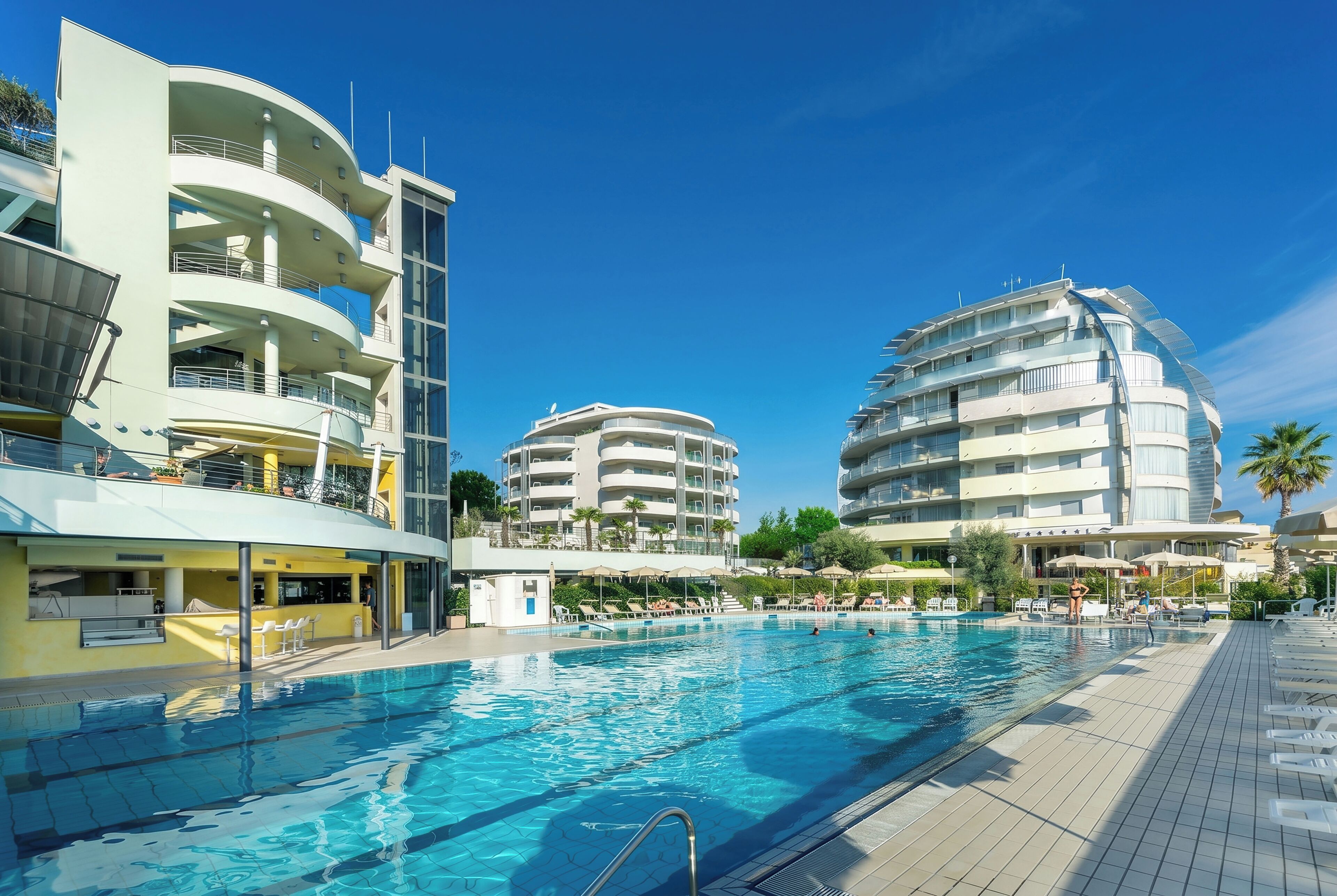 A swimming pool surrounded by modern buildings with balconies and outdoor seating areas.