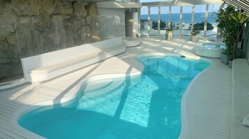 Ein Pool mit geschwungener Form, einer Steinmauer und Blick aufs Meer.