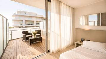Habitación de hotel con balcón, cama, una pequeña mesa con sillas y vista a un edificio.