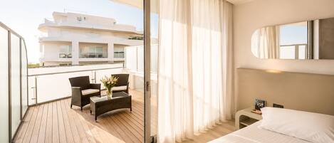 A hotel room with a balcony, a bed, a small table with chairs, and a view of a building.