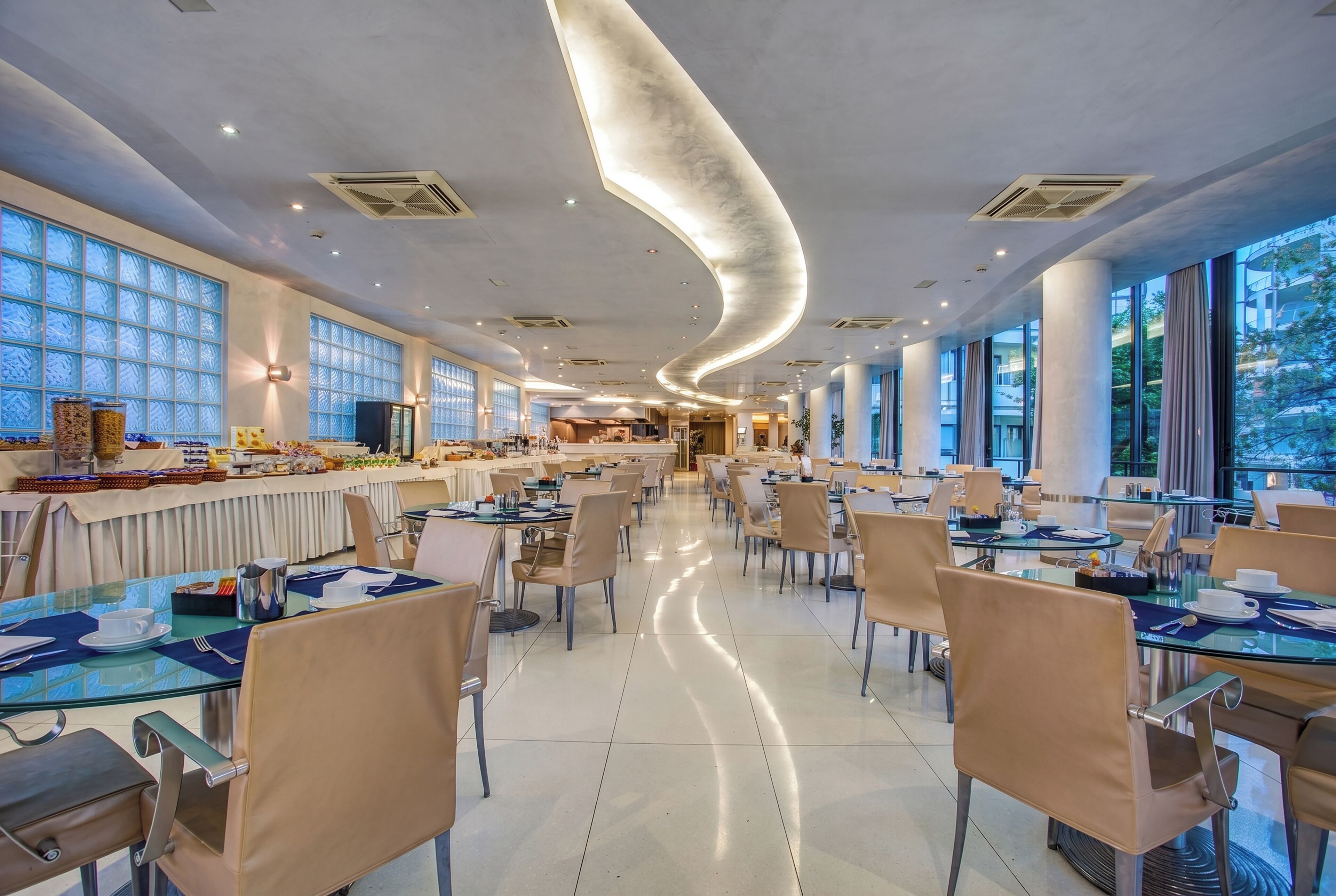 A spacious dining area with tables and chairs, large windows, and a curved ceiling design.