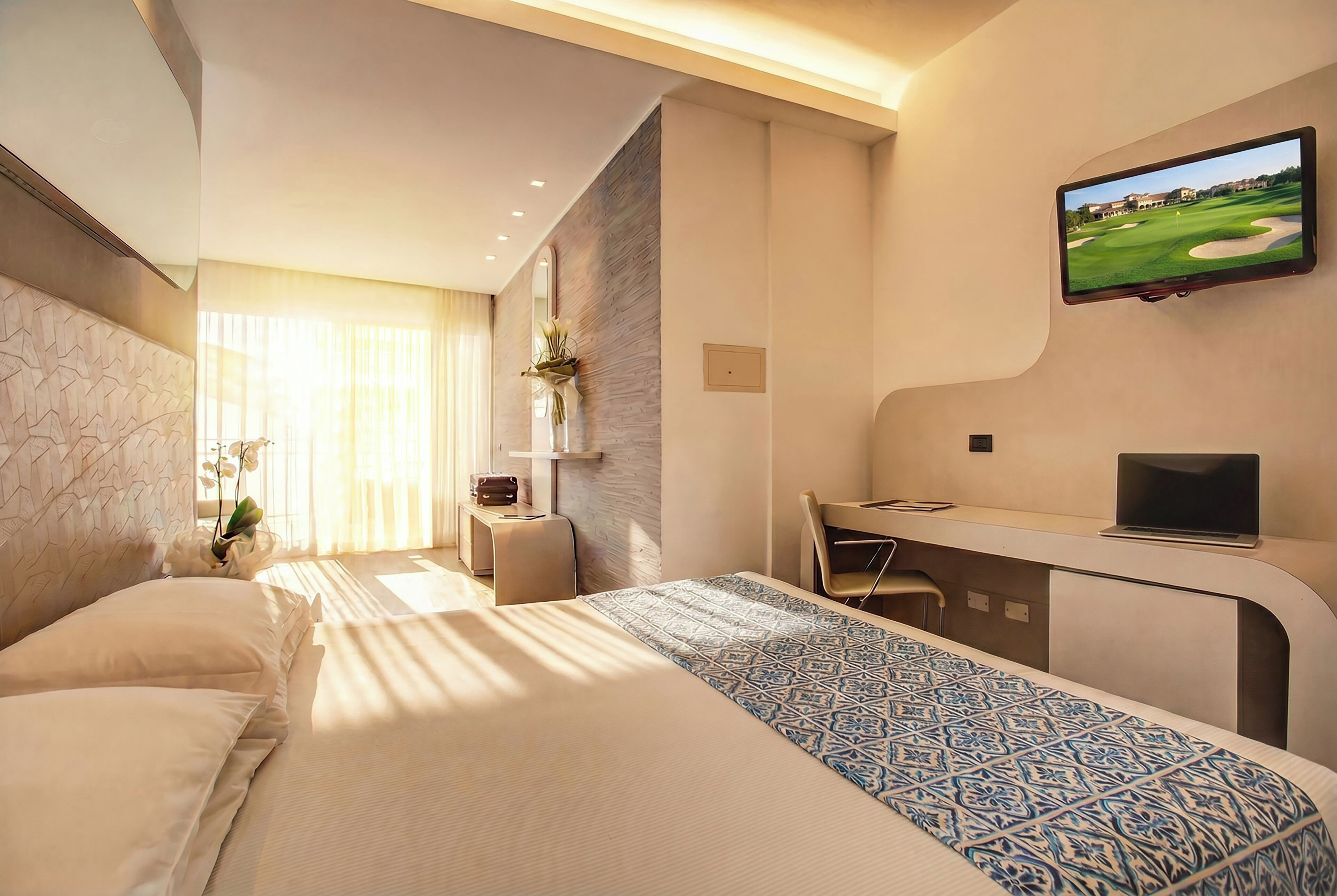 A hotel room with a bed, desk, TV, and a view of a golf course.