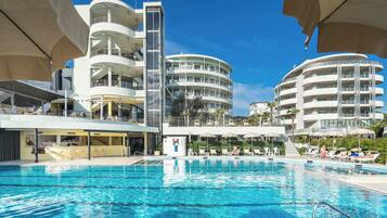A swimming pool with a modern building in the background, featuring multiple balconies and a clear blue sky.
