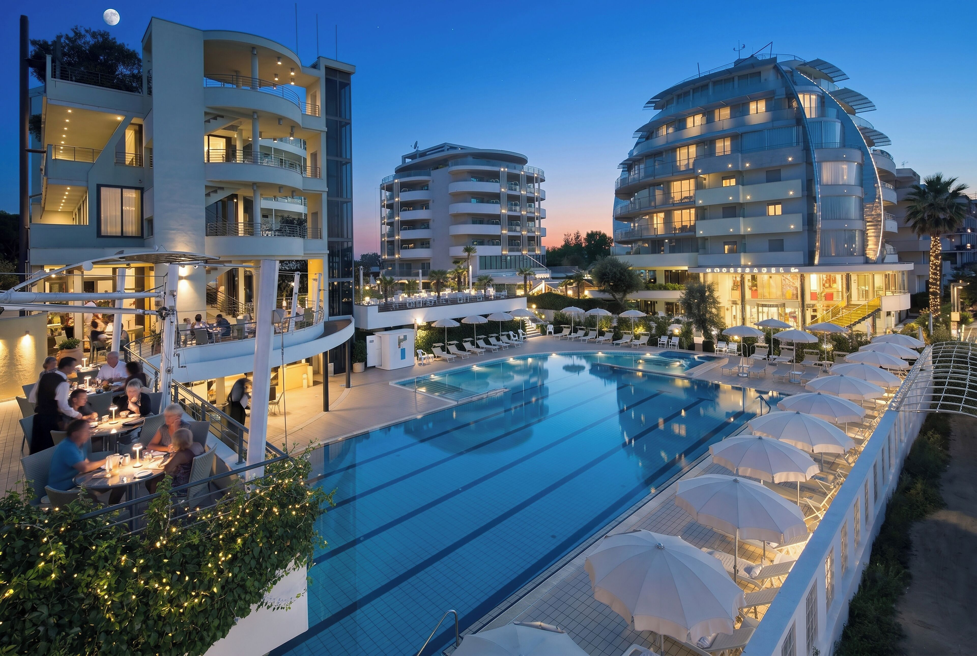 A hotel with a swimming pool, outdoor seating, and multiple balconies.