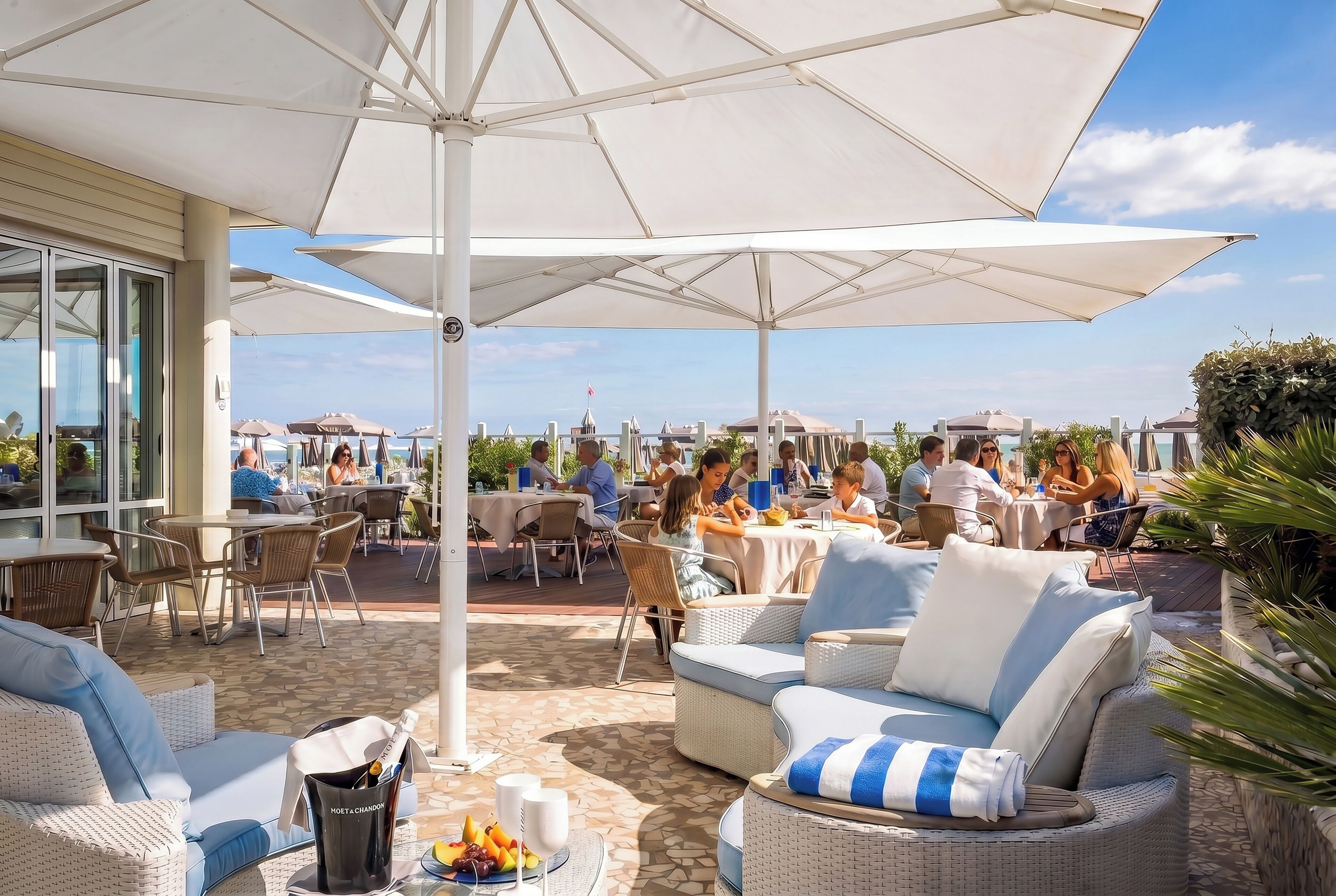 Een terras buiten met tafels, stoelen, parasols en uitzicht op zee.