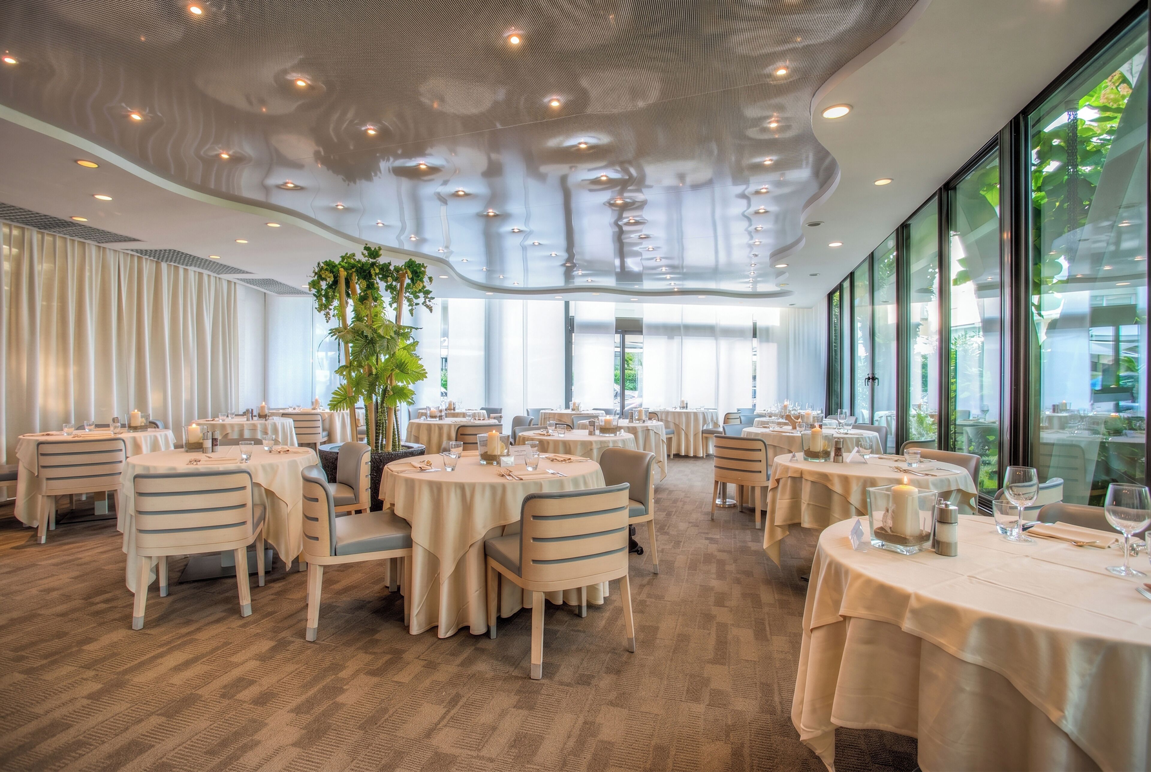 Un restaurante con mesas redondas, sillas y un techo de diseño original.