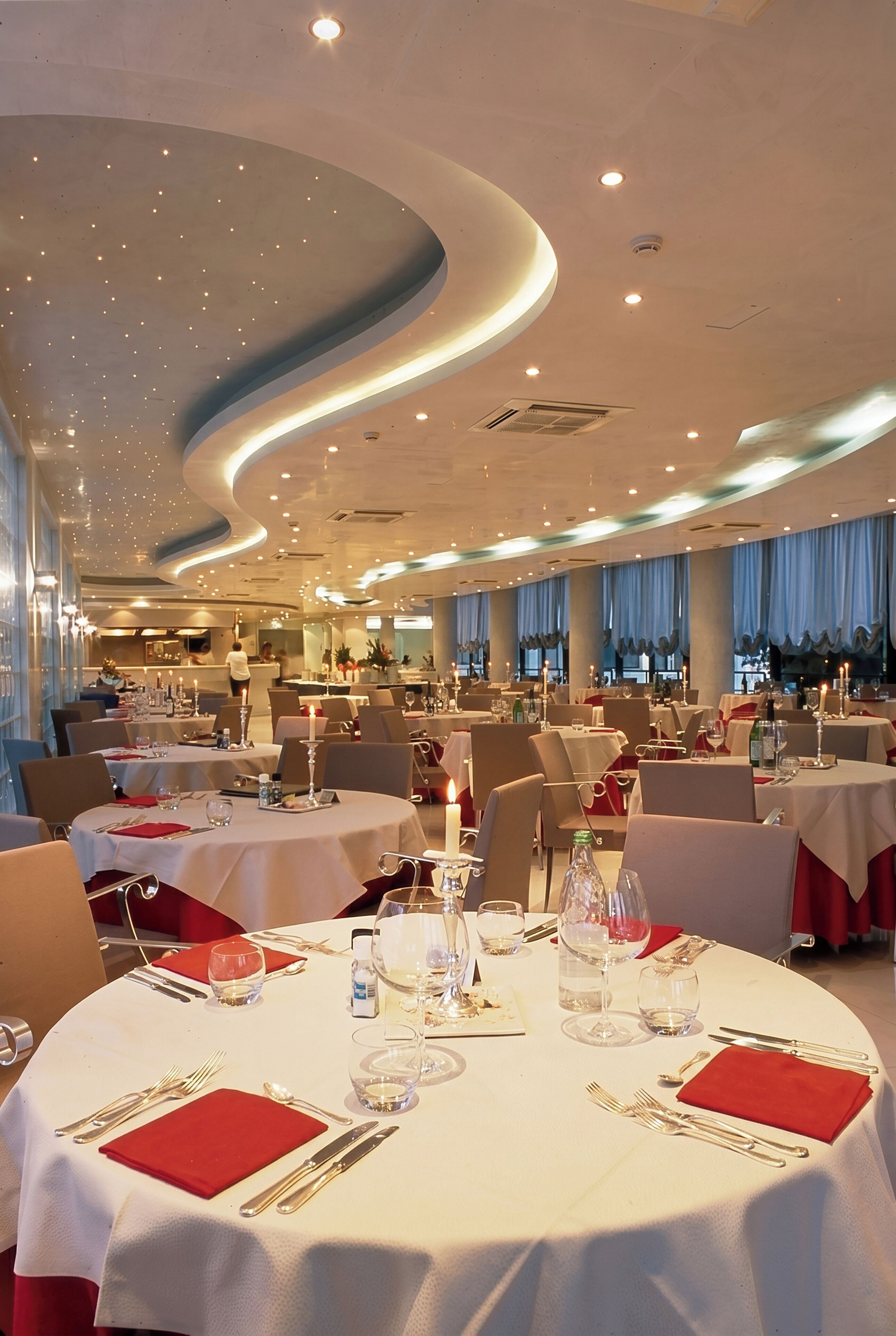 Un vaste espace dédié à la salle à manger, avec des tables rondes, des serviettes rouges et des nappes blanches.