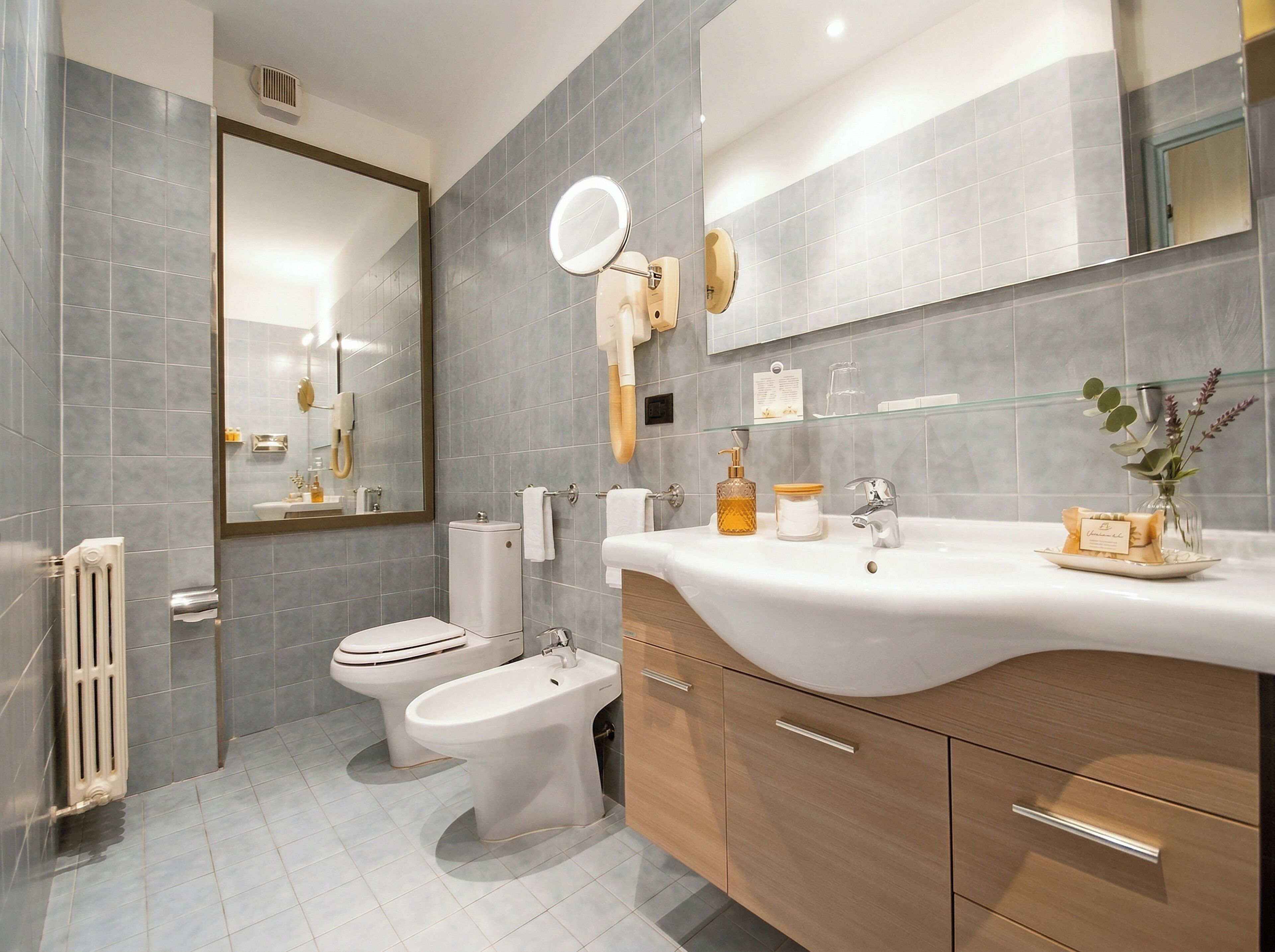 Un baño moderno con inodoro, bidé, tocador con espejo y repisa de vidrio con artículos de aseo.