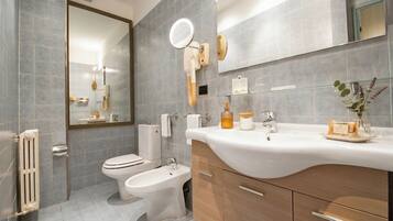 Un baño moderno con inodoro, bidé, tocador con espejo y repisa de vidrio con artículos de aseo.