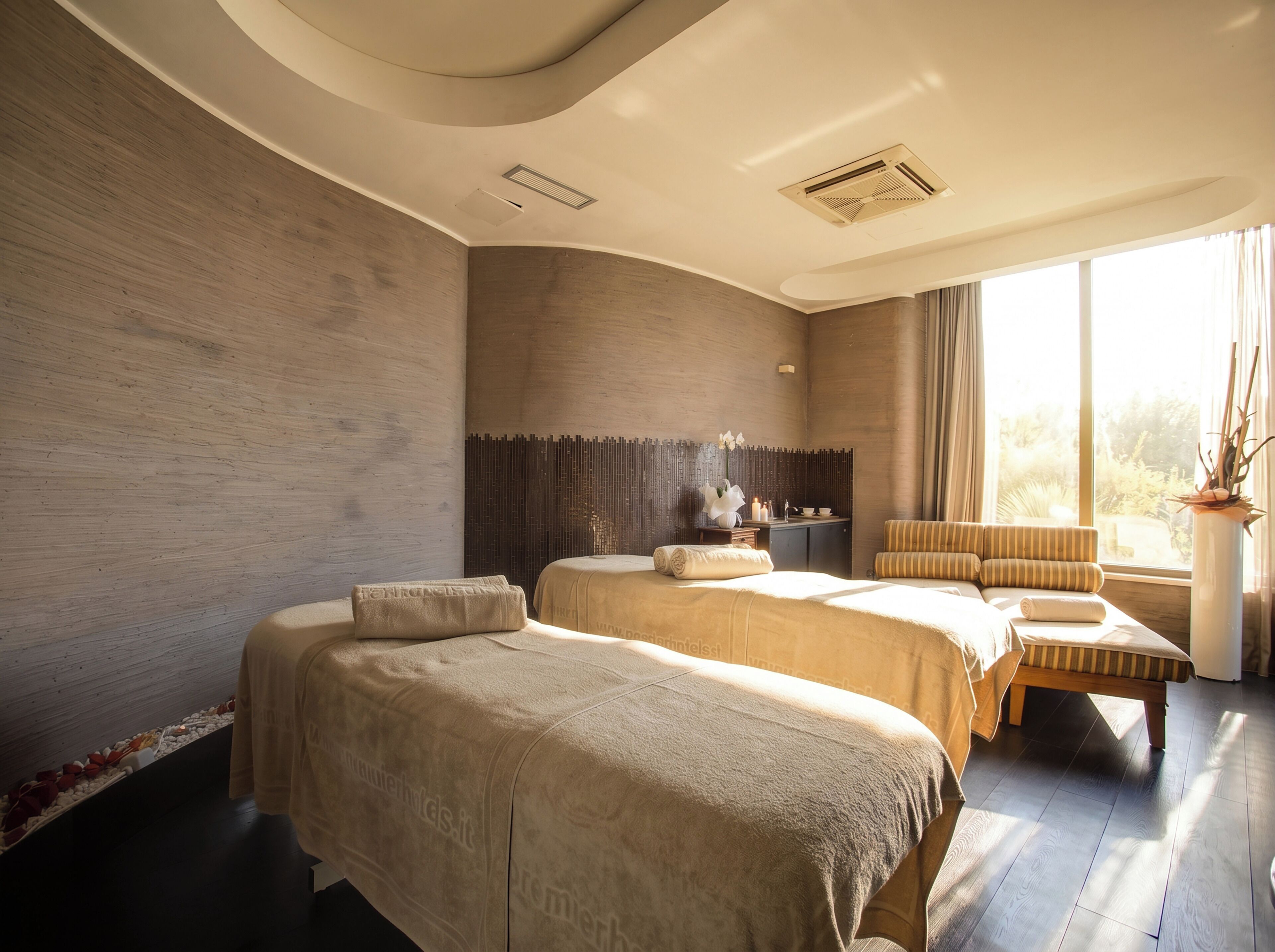 A hotel room with two beds, a sitting area, a window with curtains, and a plant.