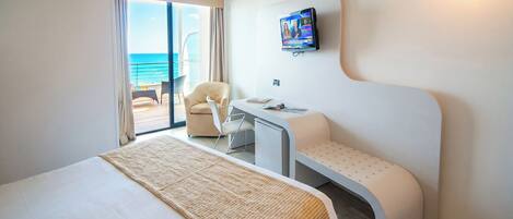 A hotel room with a bed, a desk, a chair, a television, and a view of the ocean.