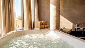 A spa room with a hot tub, beige curtains, a wooden wall, and a seating area with cushions. - Hotel Le Palme (Cervia)
