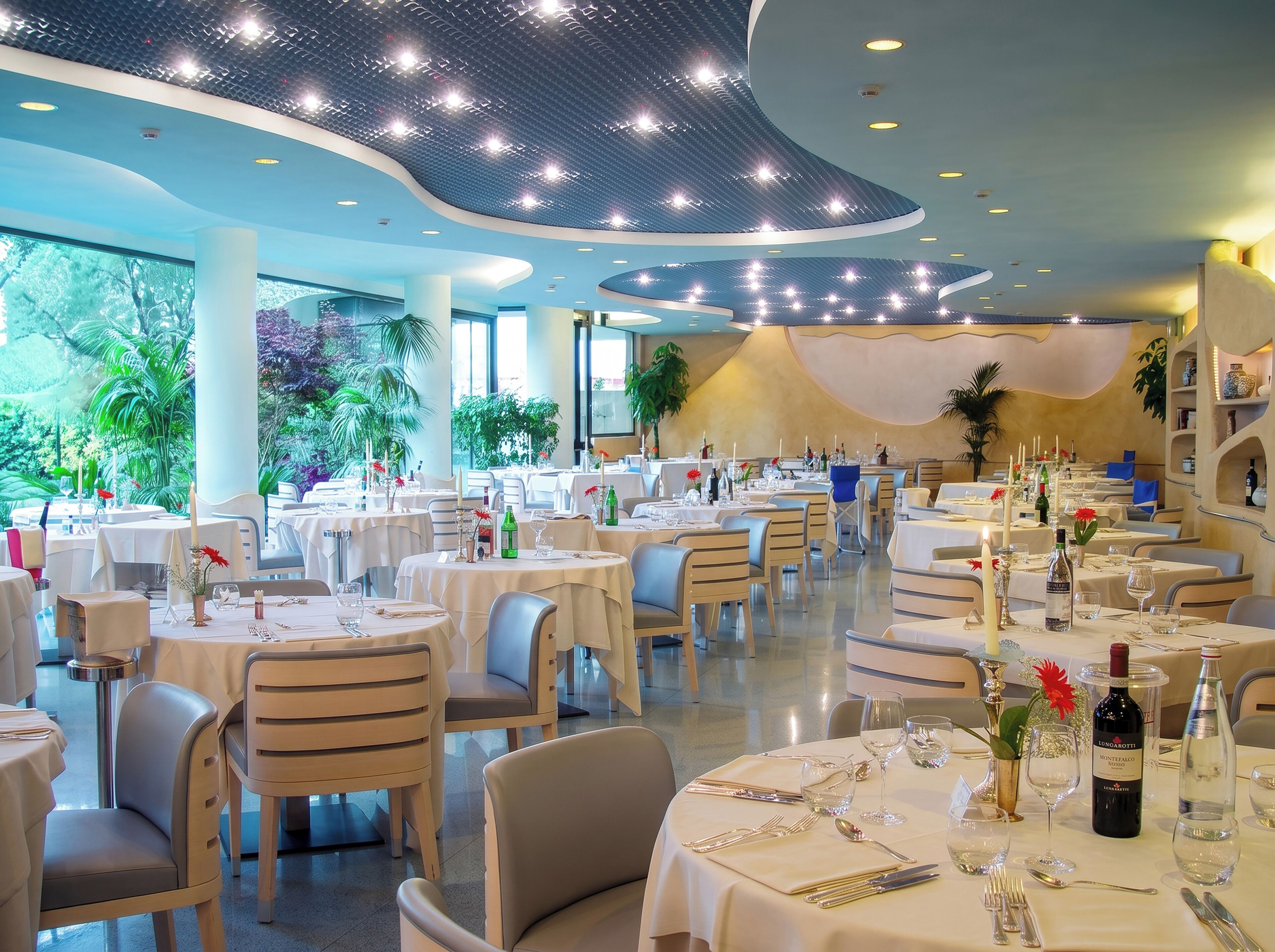 A restaurant with round tables, chairs, and a ceiling with lights.