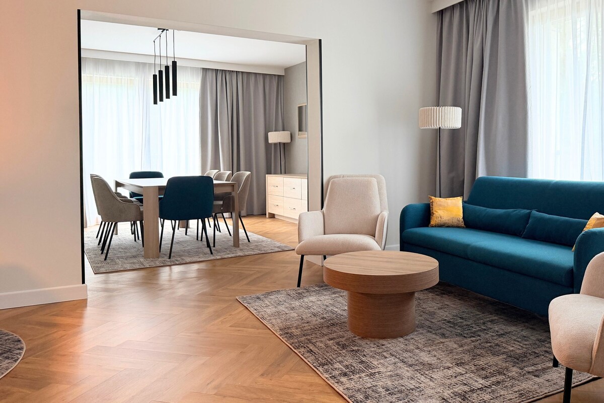 A modern living room with a blue sofa, a round coffee table, and a dining area with a table and chairs.