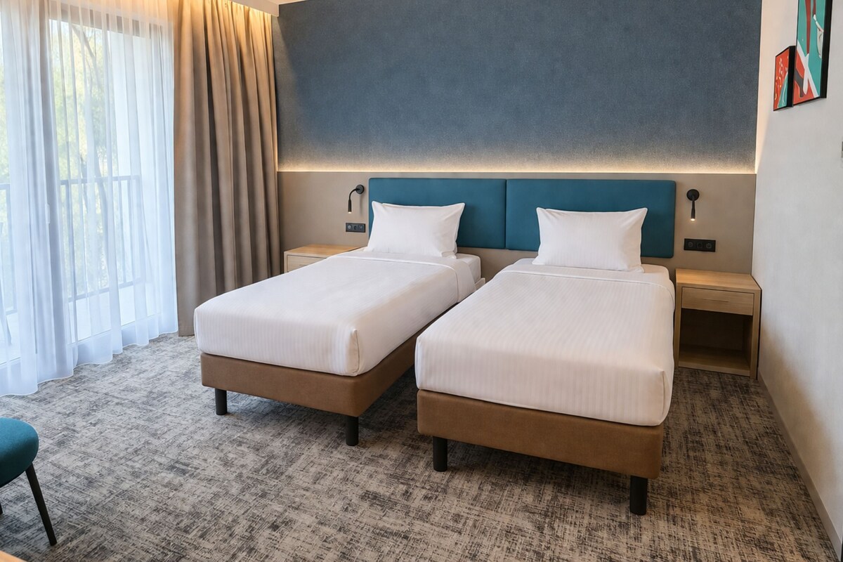 A hotel room with two beds, a desk, a chair, and a view of the outdoors.