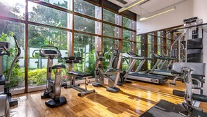 Une salle de sport équipée de machines de cardio, de postes de musculation et dotée d’une grande fenêtre donnant sur un espace verdoyant.