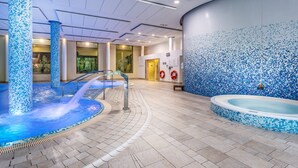 Un espace piscine intérieure doté d’un sol carrelé, d’un jacuzzi et d’une rambarde en verre.