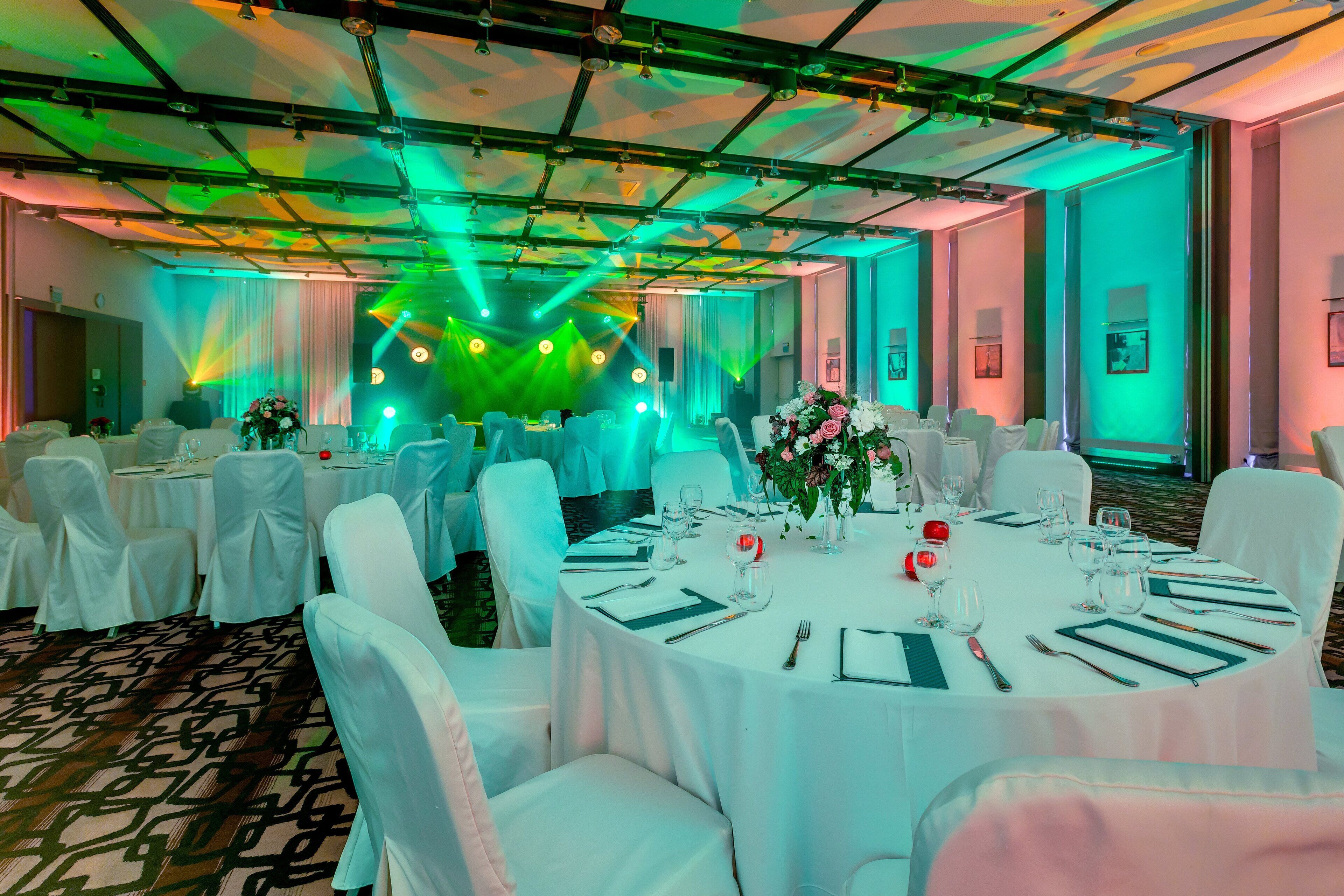 A banquet hall with round tables set for dining, white chairs, and tables covered with white tablecloths.