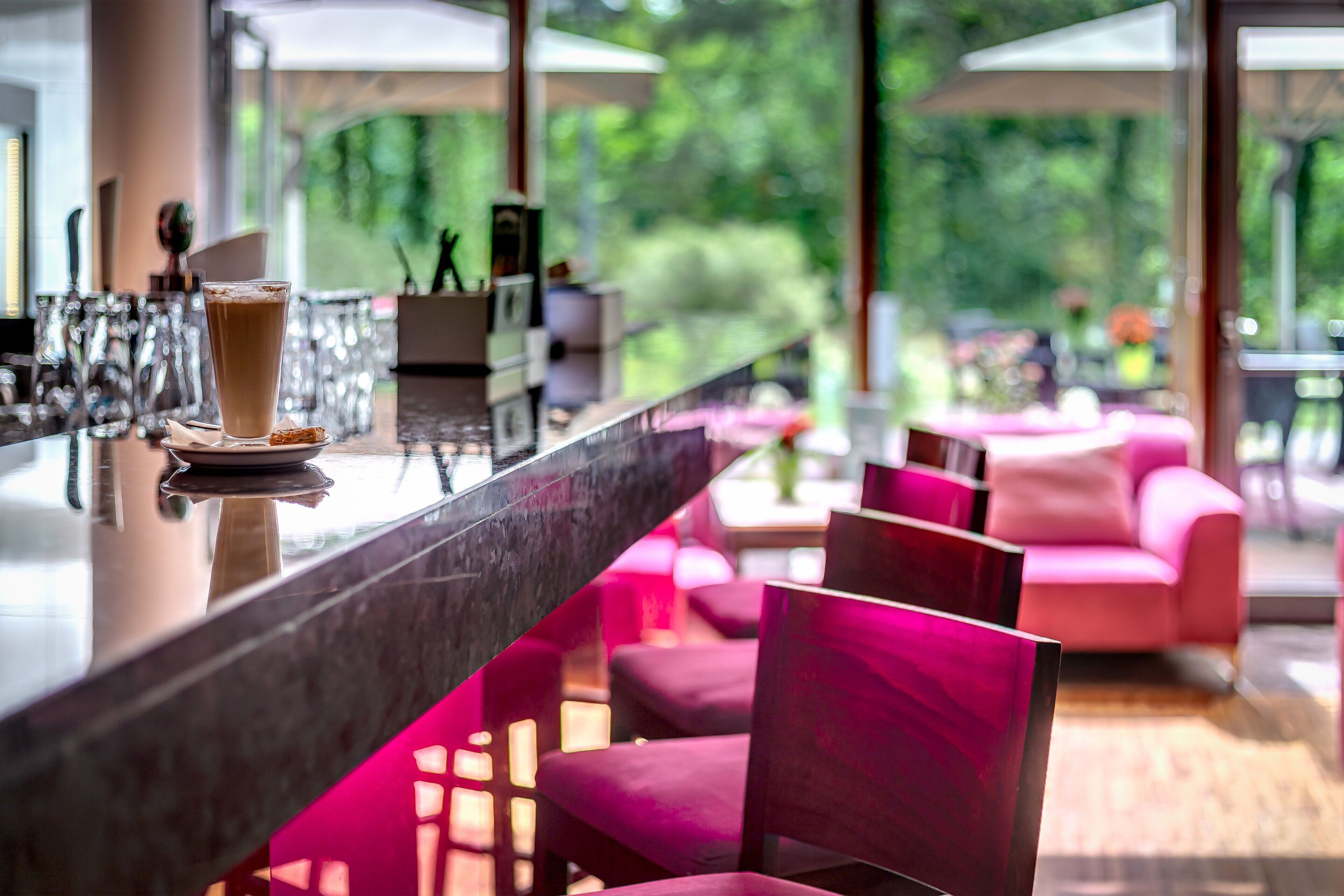 A bar area with a glass of a beverage, a marble countertop, and pink chairs in the background.