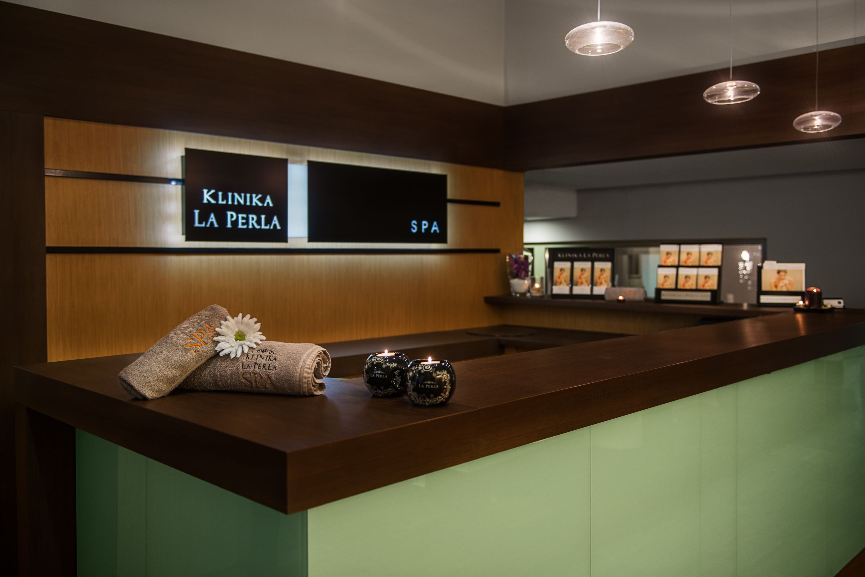 A reception area with a sign reading "Klinska La Perla SPA," a wooden reception desk, and a green counter.