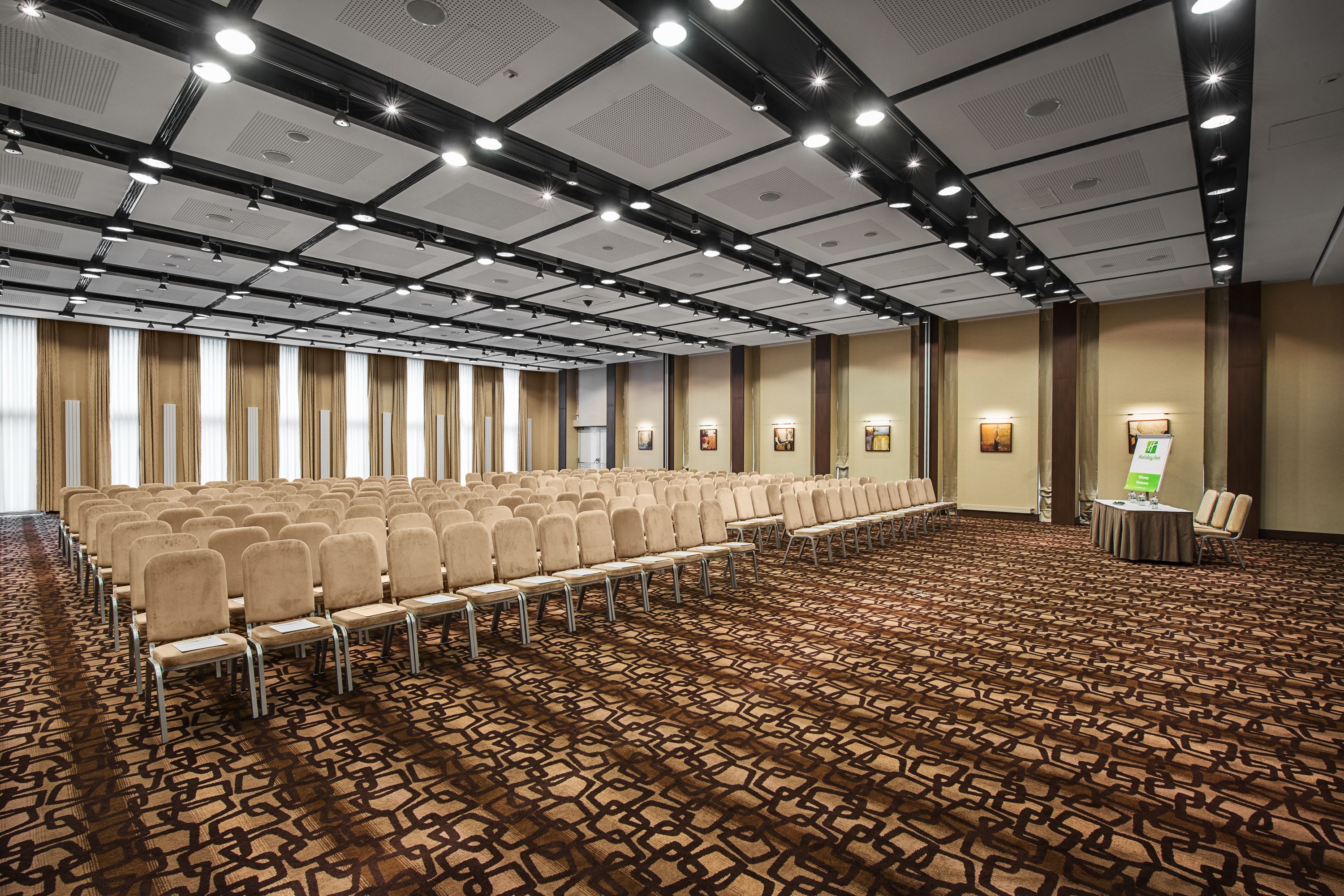 A conference room with rows of chairs, a patterned carpet, and a ceiling with recessed lighting.