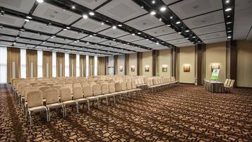 A conference room with rows of chairs, a patterned carpet, and a ceiling with recessed lighting.