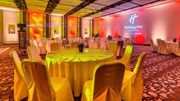 A conference room with round tables, yellow chairs, and a large screen displaying the Holiday Inn logo.