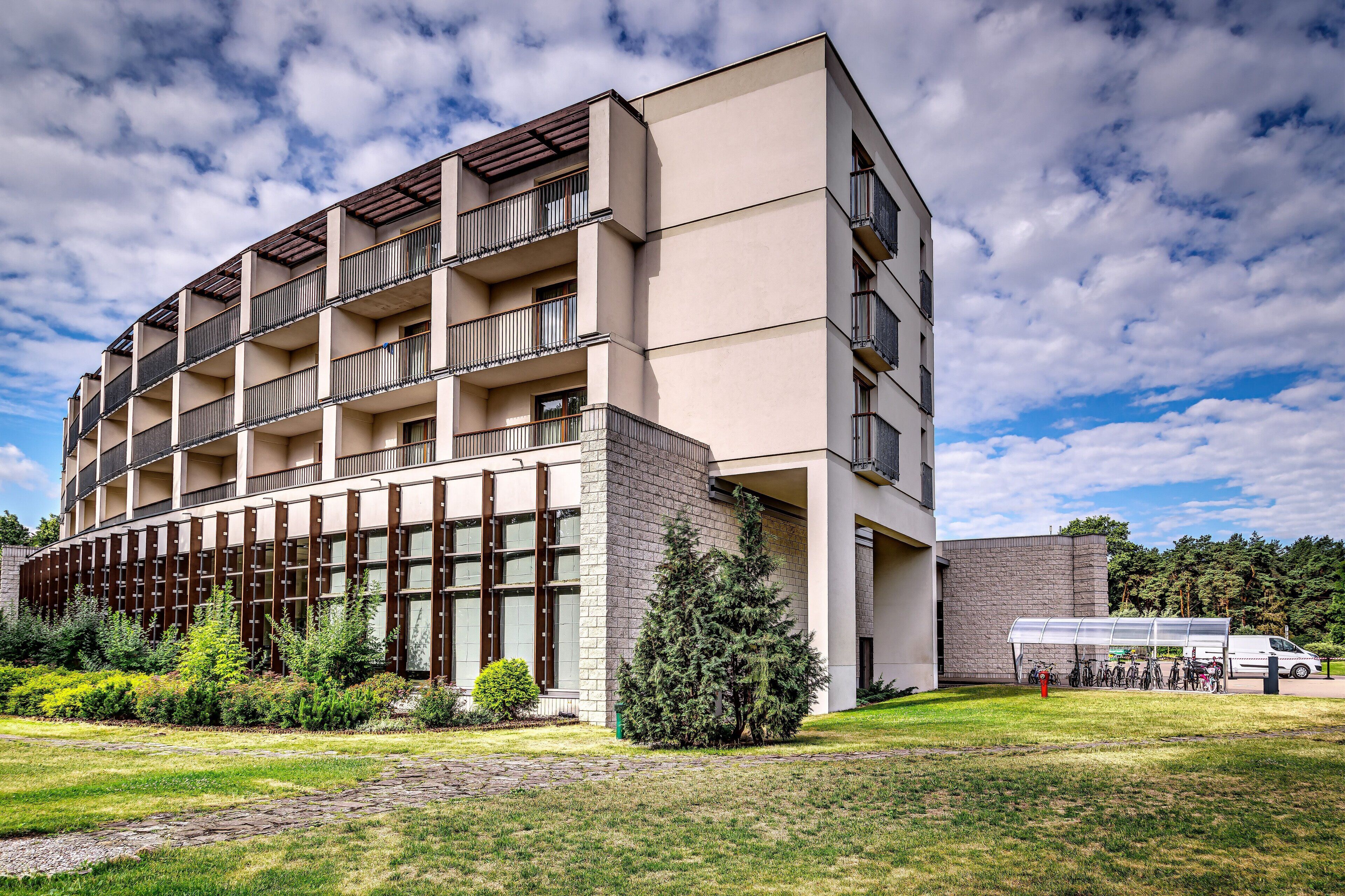 Un edificio moderno de varios pisos con balcones, un espacio cubierto para bicicletas y un patio con césped.