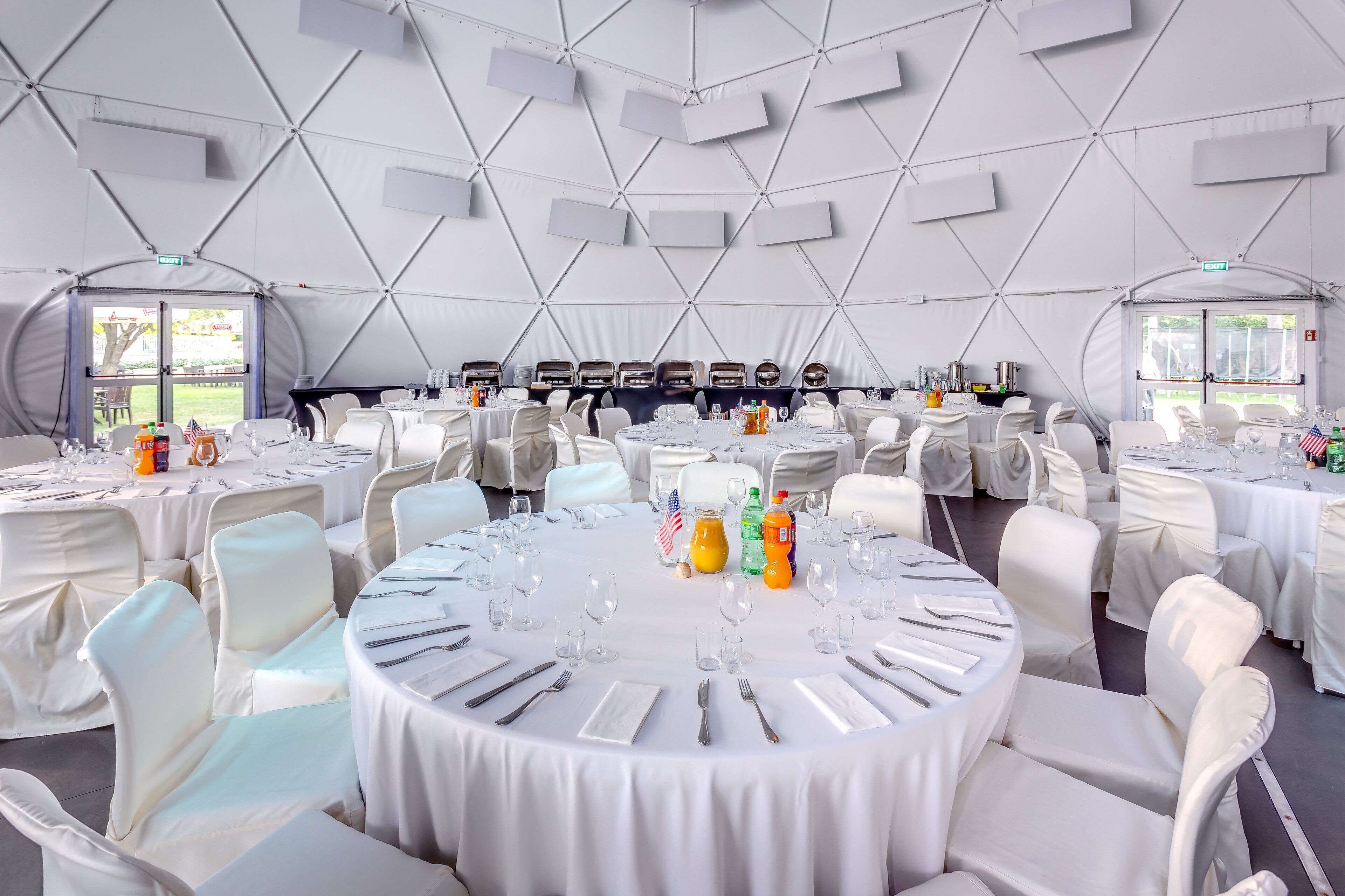 A large, tented event space with round tables set for dining, white chairs, and a central stage area.