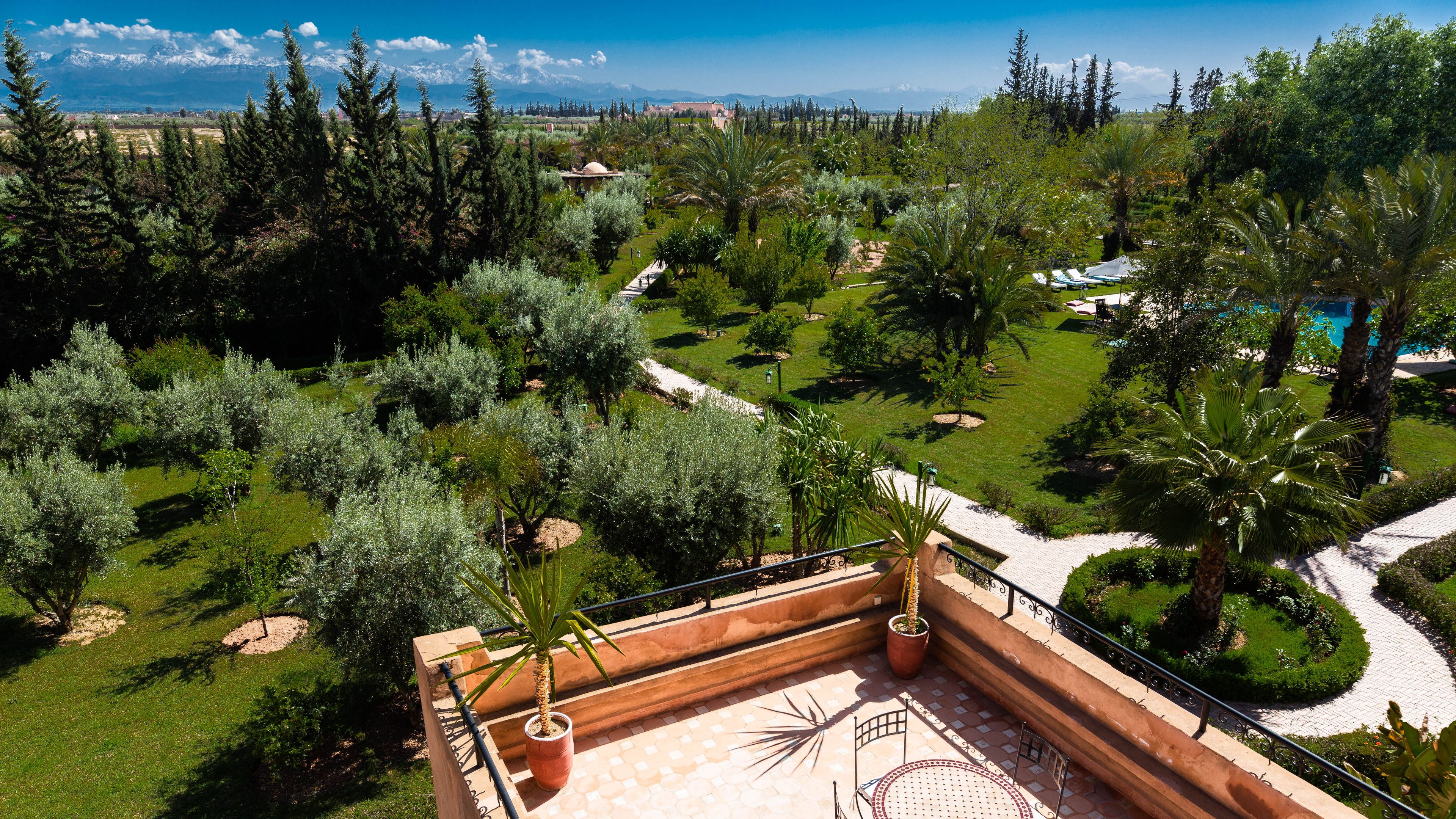 Una terraza en la azotea con vistas a un jardín ajardinado, una zona de piscina y montañas a lo lejos.