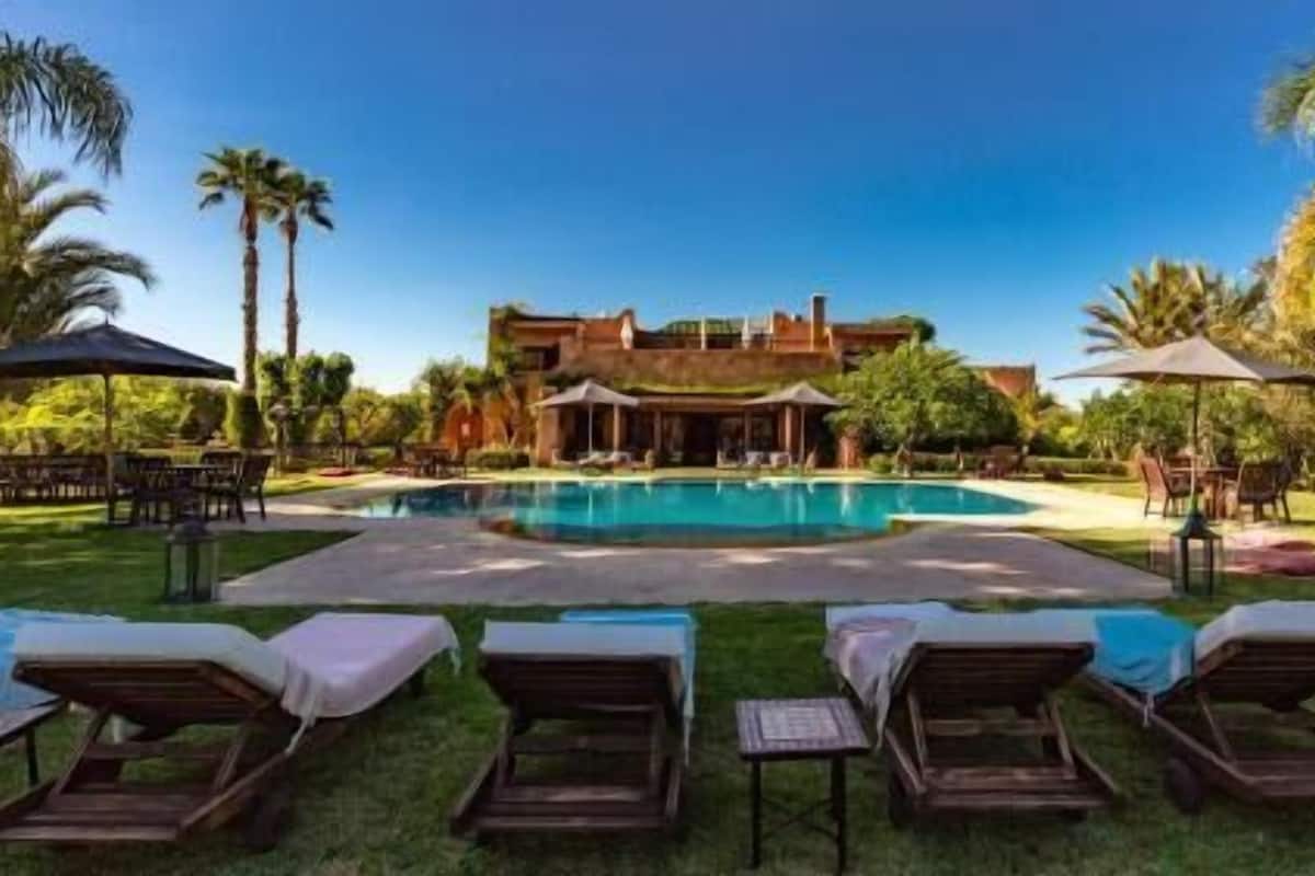 A pool with lounge chairs, a building with a red facade, and palm trees.