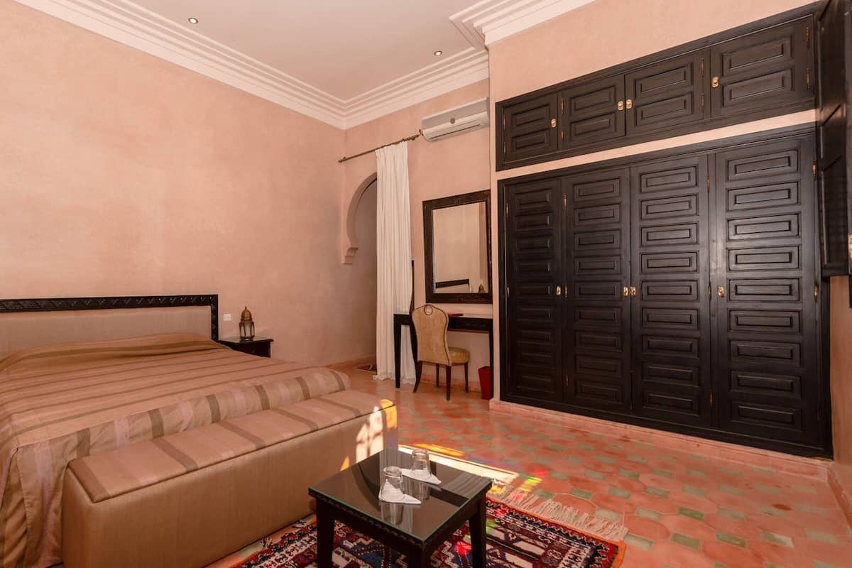 A bedroom with a bed, a desk, a chair, a wardrobe, and a small table with glasses.