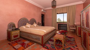 Un dormitorio con una cama grande, un cabecero ornamentado, una mesita de noche con un florero de flores rojas y un mueble decorativo.