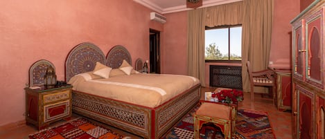A bedroom with a large bed, ornate headboard, a small table with a vase of red flowers, and a decorative cabinet.