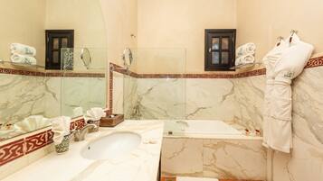 A bathroom with a marble sink, a bathtub, and a large mirror. There are towels and toiletries on the counter.