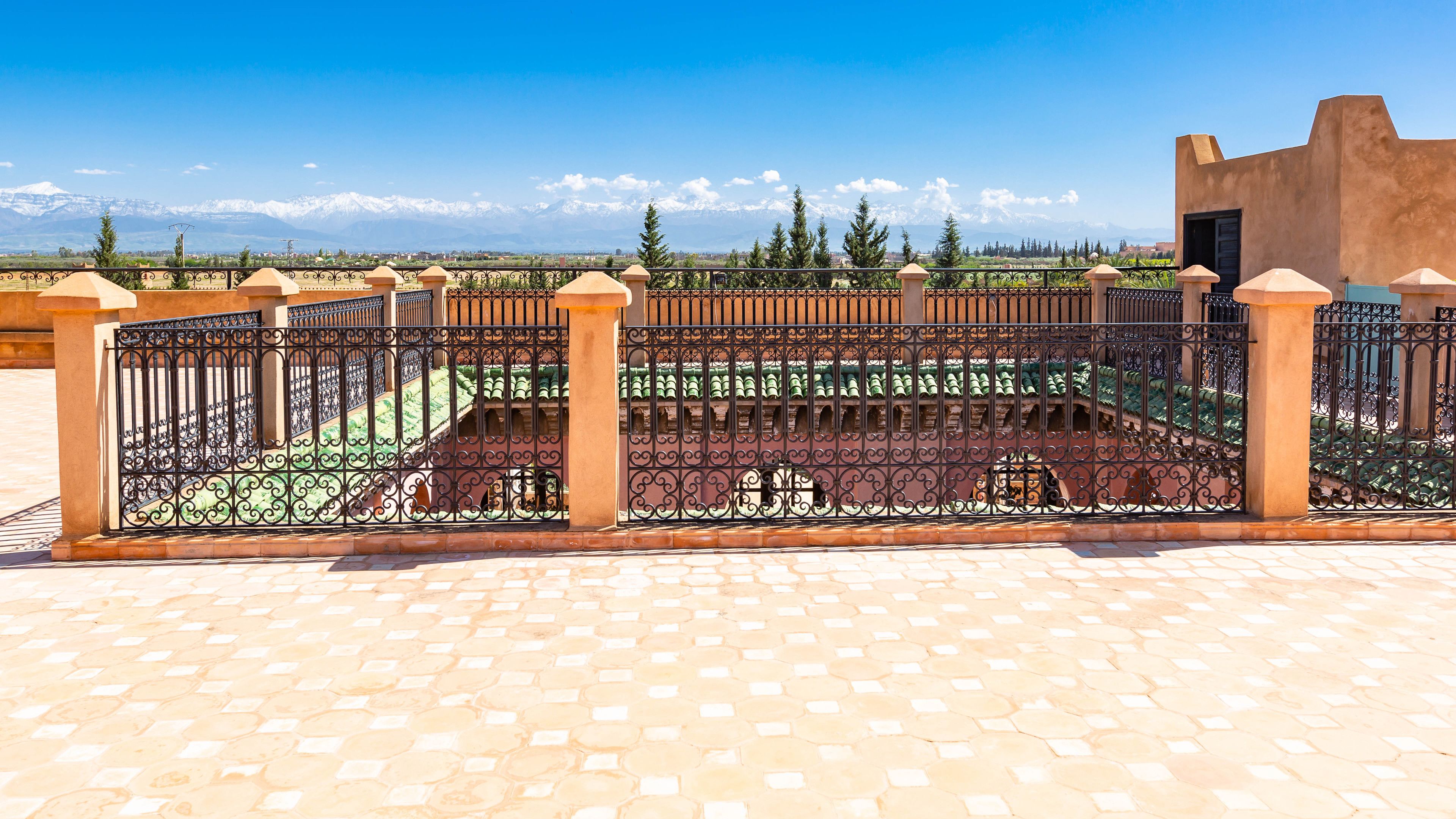 A courtyard with a wrought iron fence, a tiled floor, and a view of snow-capped mountains in the background.