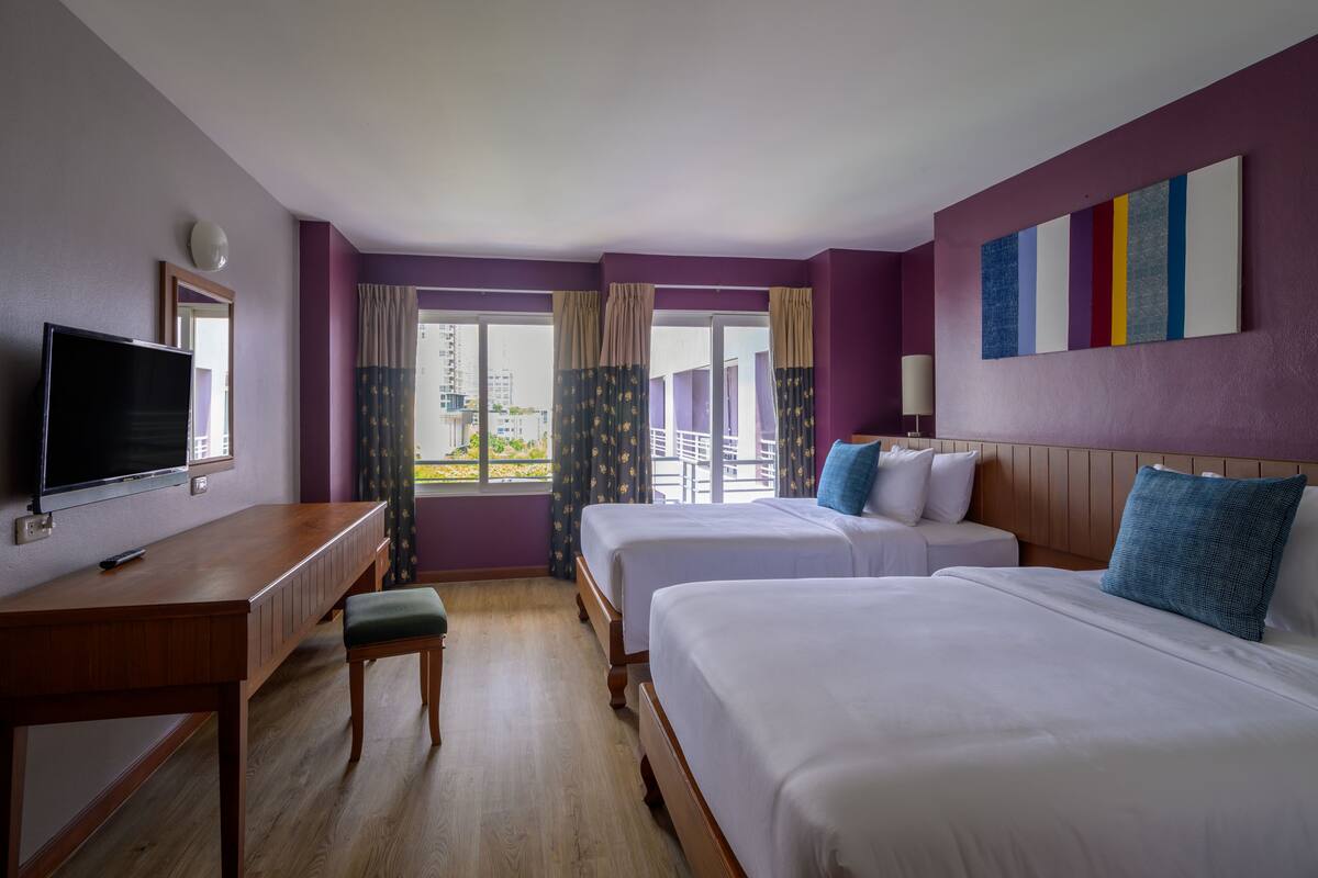 A hotel room with two beds, a desk, a TV, and a window with curtains.