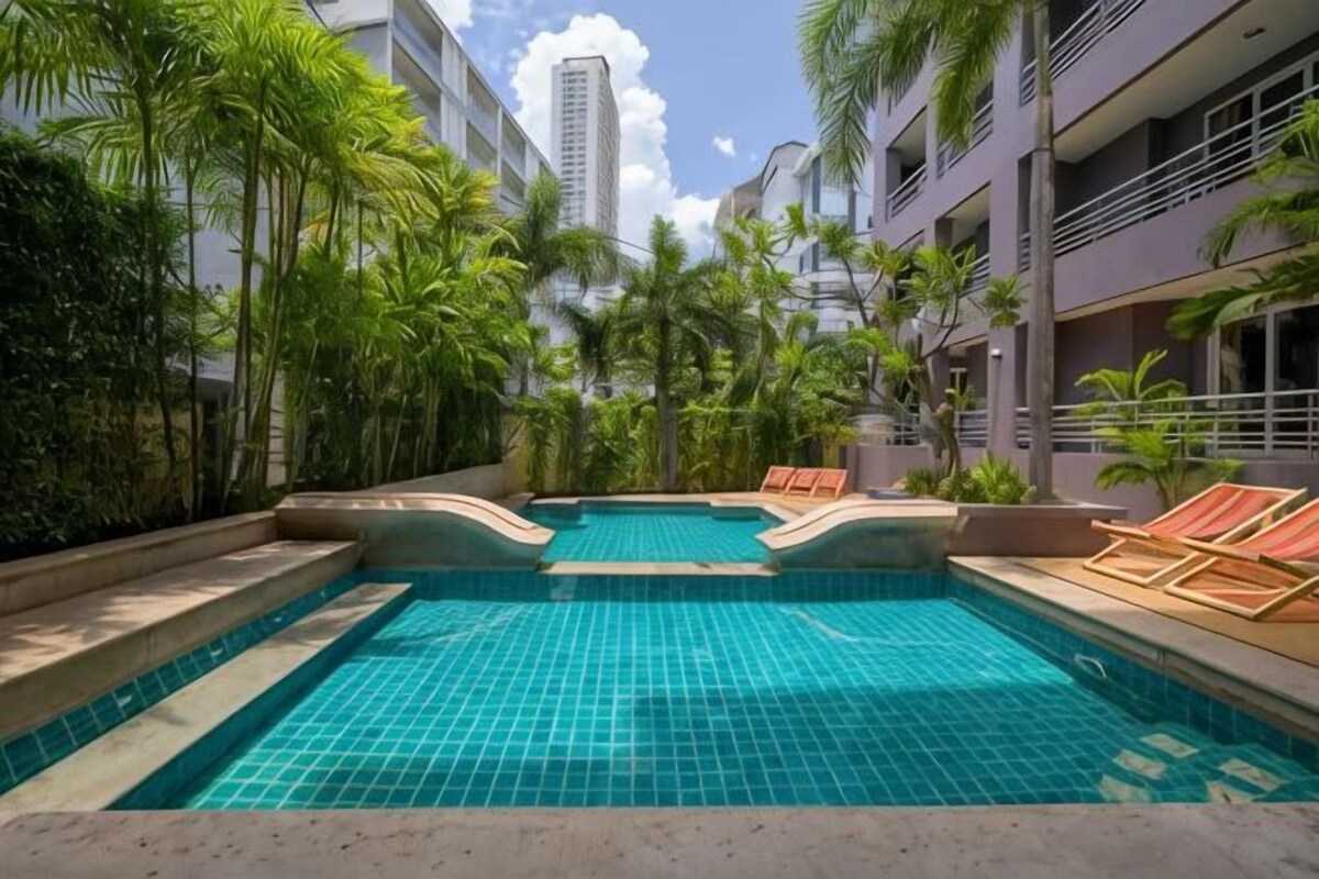 Una piscina con bordi piastrellati, circondata da palme e lettini.